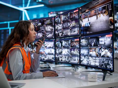 A woman in high-viz talks in to a radio handset while looking at CCTV monitors.