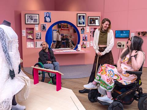 Two wheelchair users and a person with a walking stick look at museum exhibition artifacts.