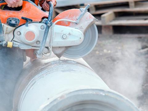 A construction worker uses a circular saw to cut a large concrete pipe.