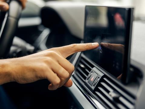 A driver reaches out to interact with a built-in touchscreen on the dashboard